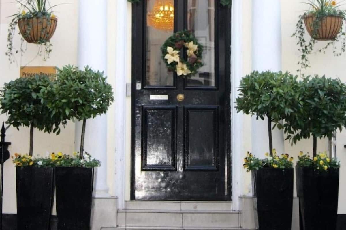 A black door with 'REEM HOTEL' above it, flanked by two potted plants and a sign reading 'Prince Square'.