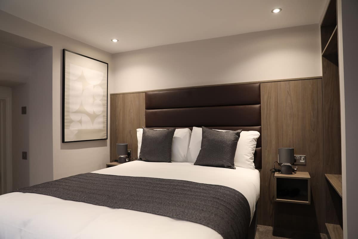 Ein modernes Schlafzimmer mit einem großen Bett, einem Kopfteil, Nachttischen und einem gerahmten Kunstwerk an der Wand.
