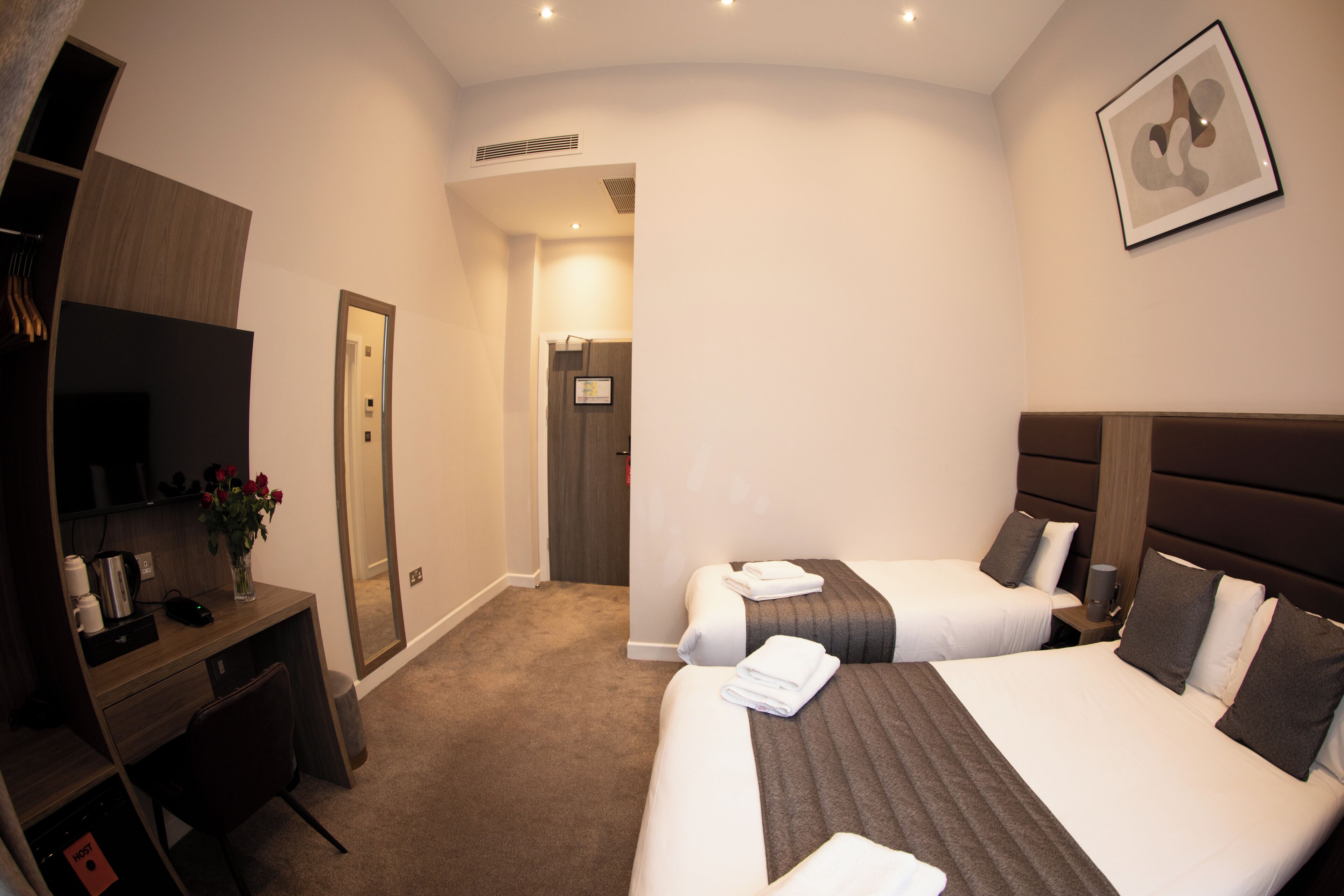 A hotel room with two beds, a desk, a chair, and a mirror.