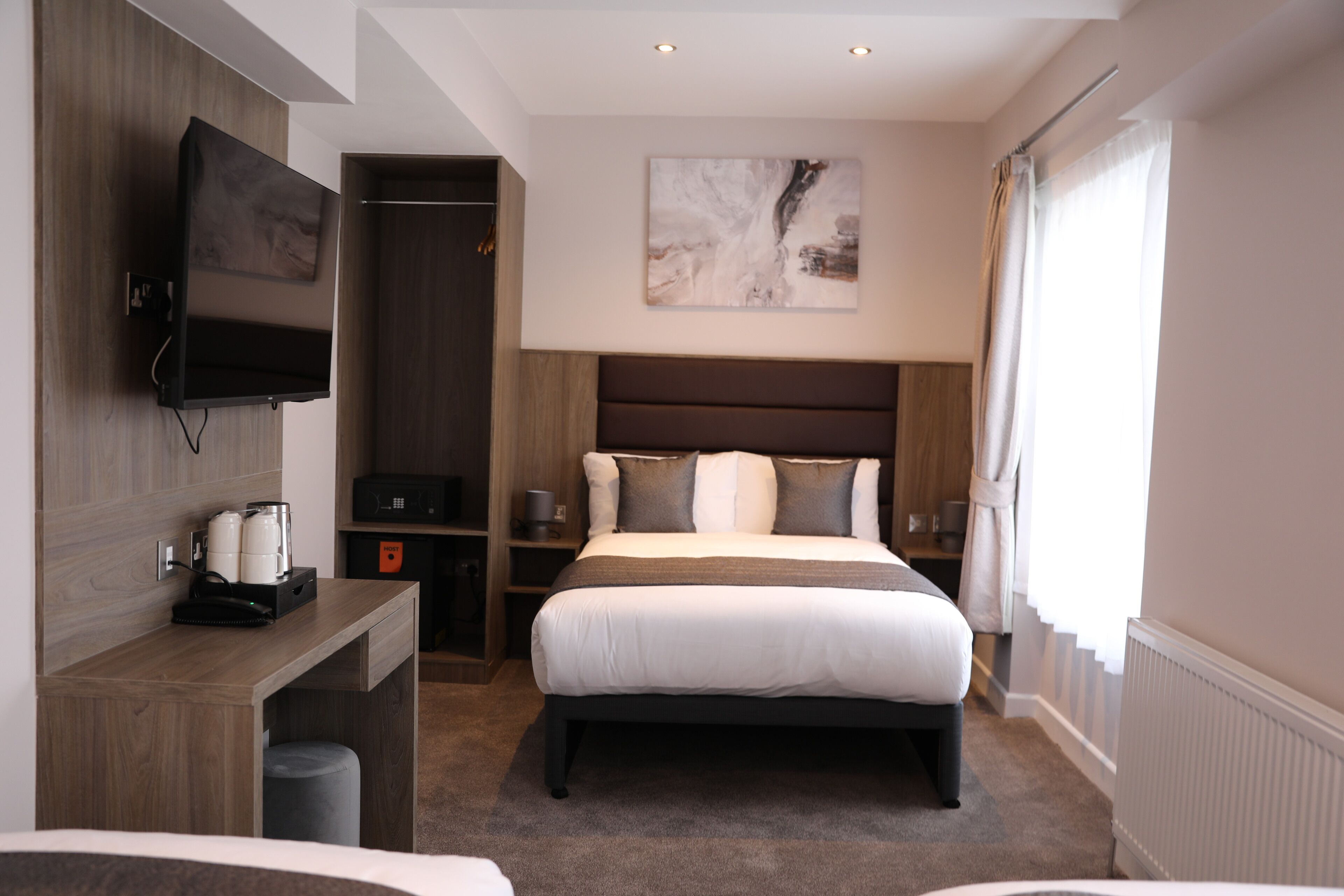 Una habitación de hotel moderna con una cama grande, un televisor de pantalla plana montado en la pared, un escritorio de madera y un ventanal con cortinas.