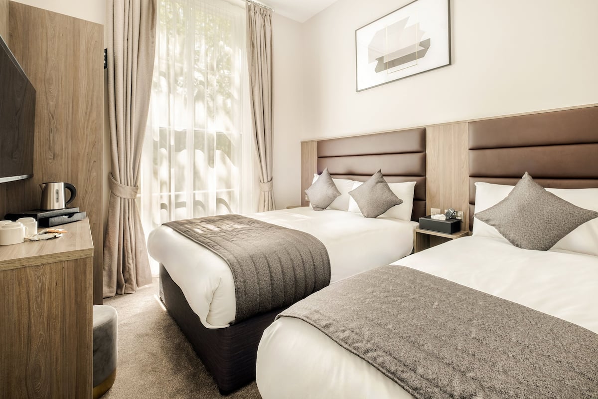 Ein Hotelzimmer mit zwei Betten, einem Holztisch, einem Fernseher und einem Fenster mit Vorhängen.