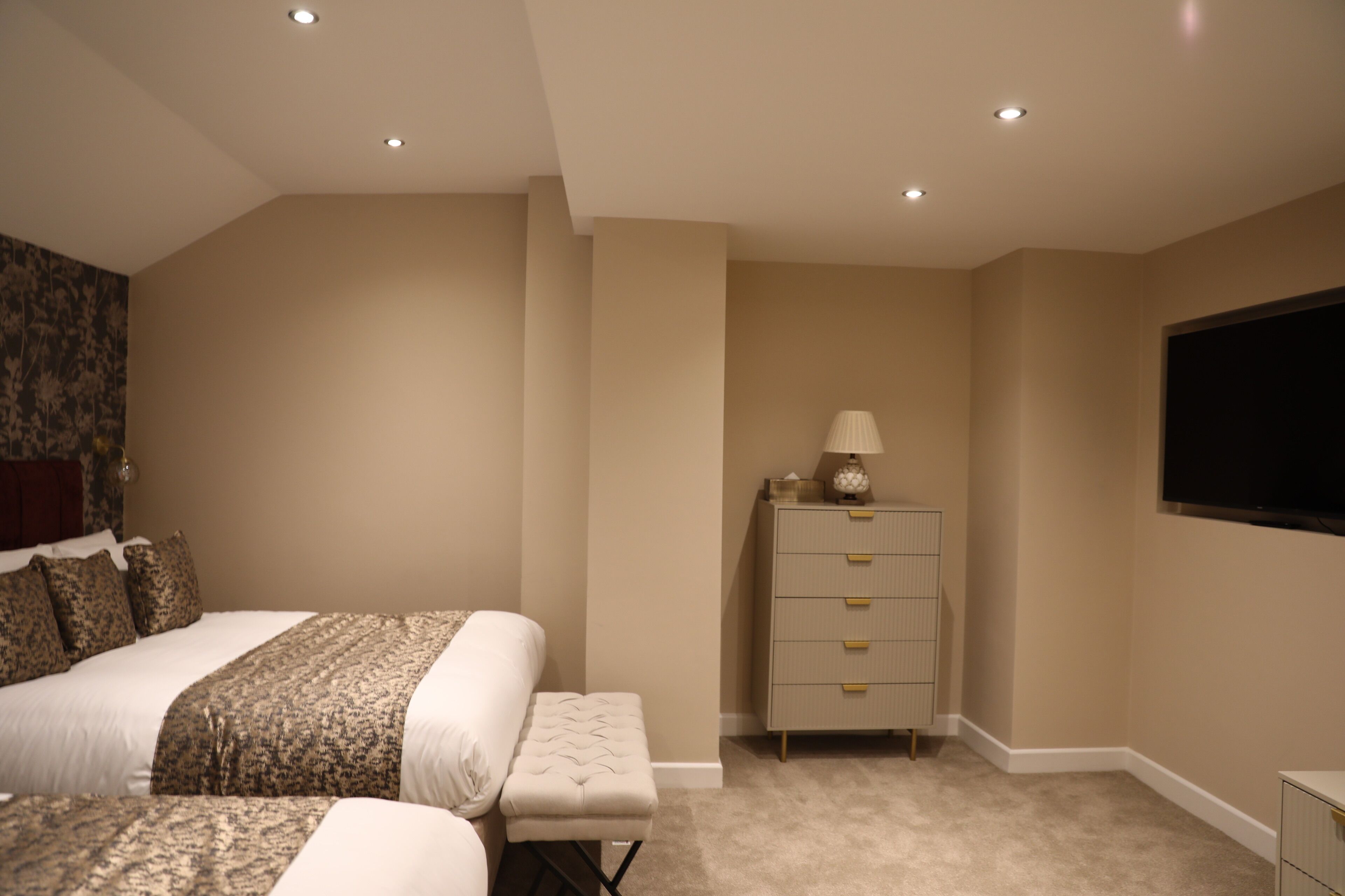 A bedroom with a bed, a nightstand, a dresser, and a television on the wall.