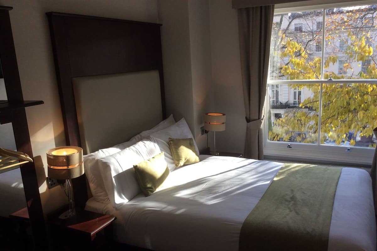 A hotel room with a large bed, bedside lamps, a window with a view of trees, and a wooden headboard.