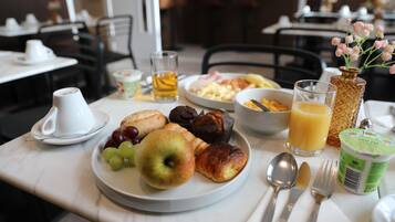Una mesa con desayuno: una fuente de frutas, croissants y un vaso de zumo de naranja.