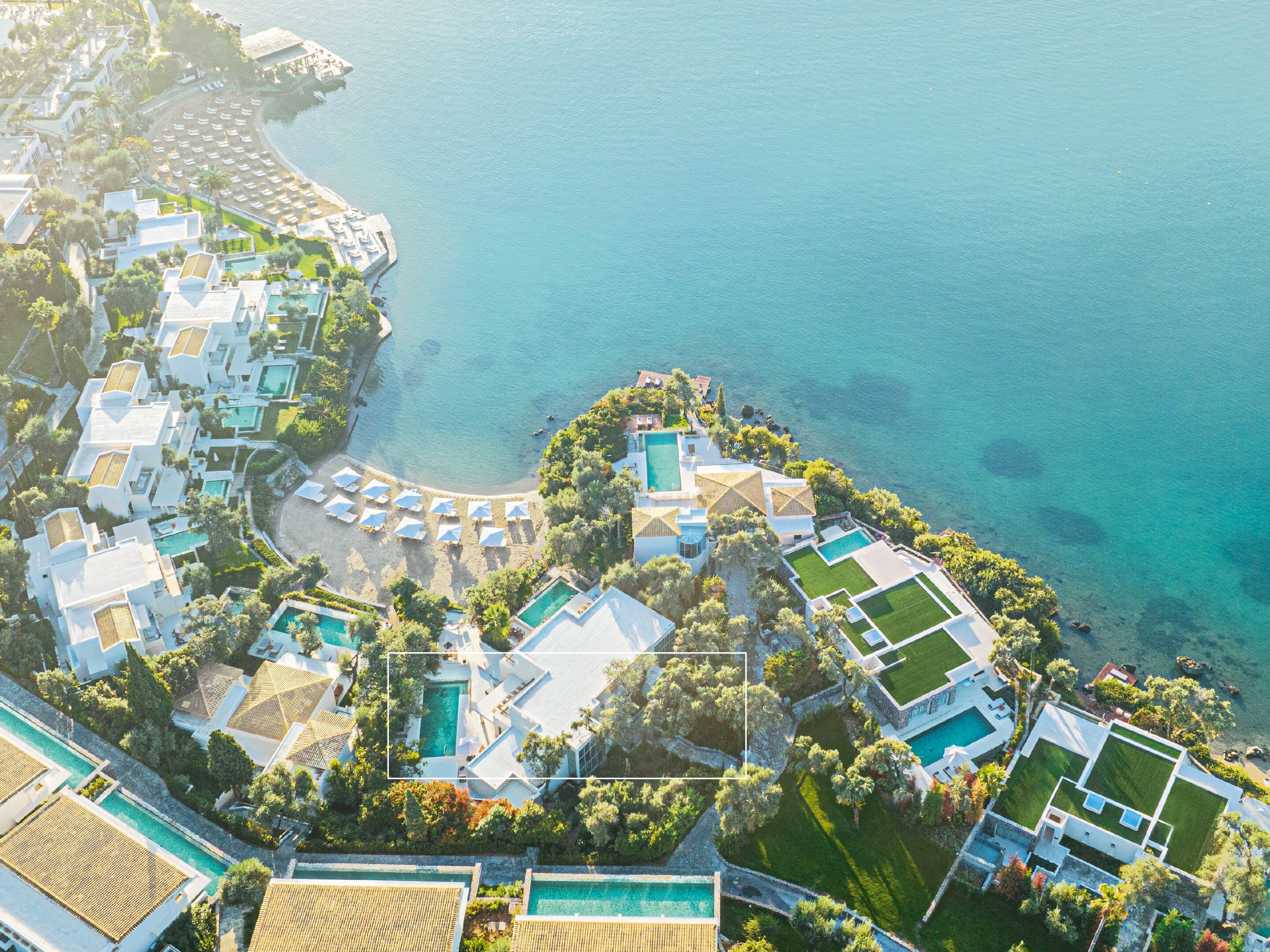An aerial view of a coastal resort with multiple buildings, swimming pools, and a beach area.