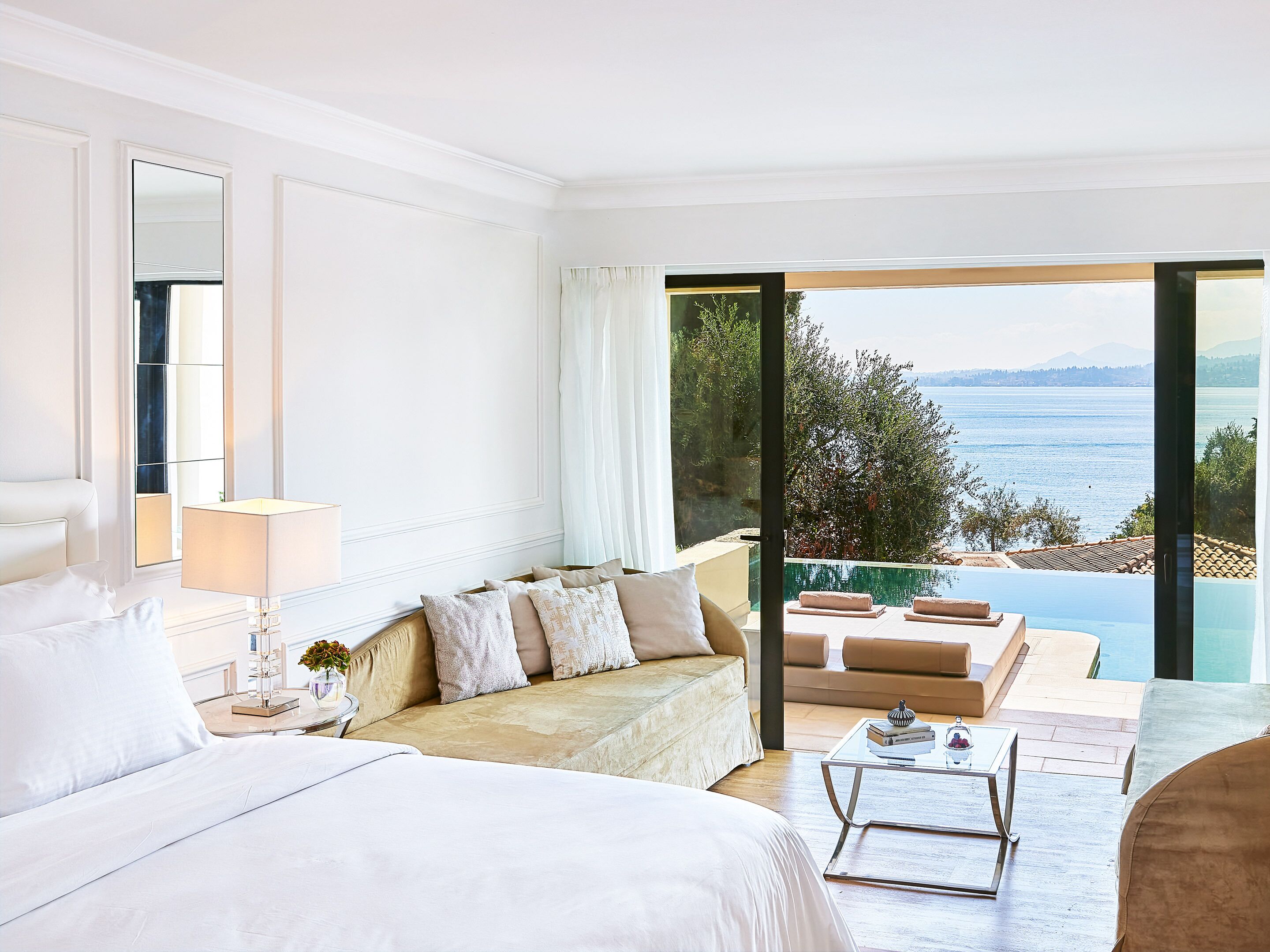 Un dormitorio amplio con una cama grande, una zona de estar con sofá y vistas a una piscina y al océano.