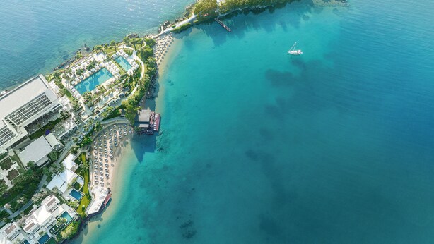 An aerial view of a coastal resort with a swimming pool, beach, and a boat dock.