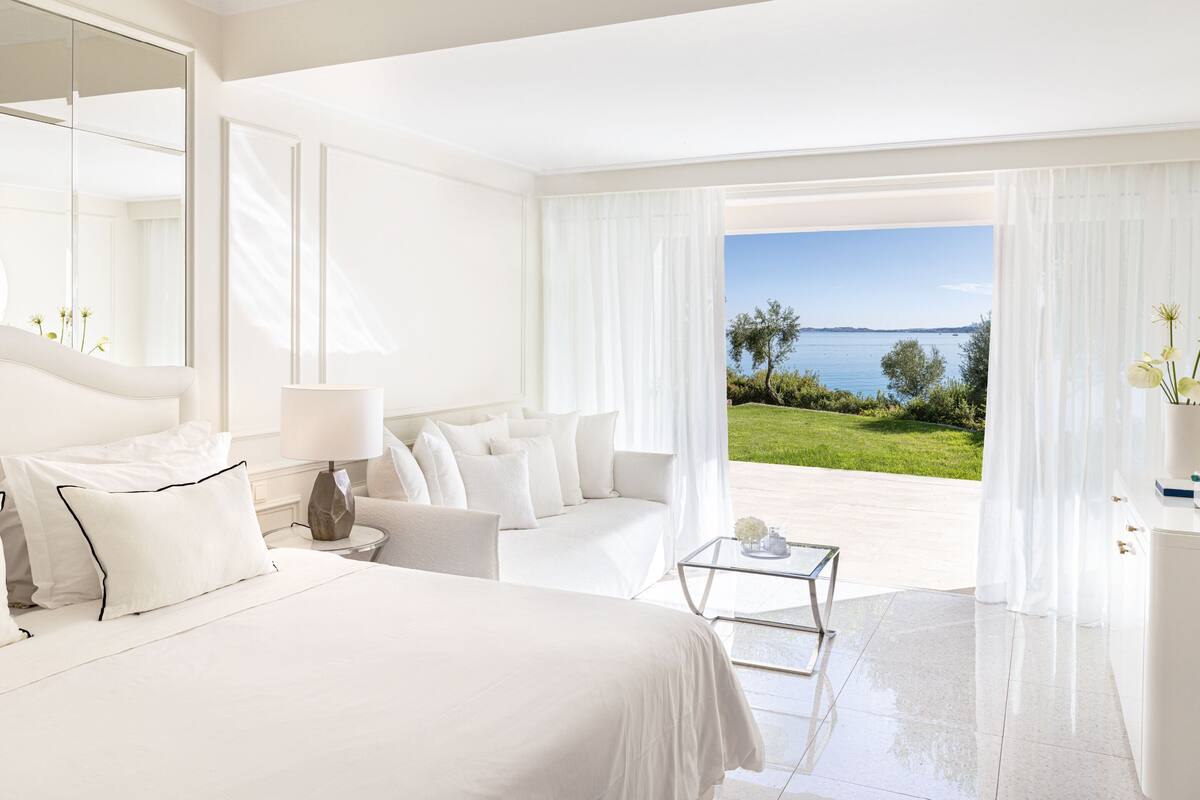 A modern hotel room with a large bed, a sitting area, and a view of the sea.
