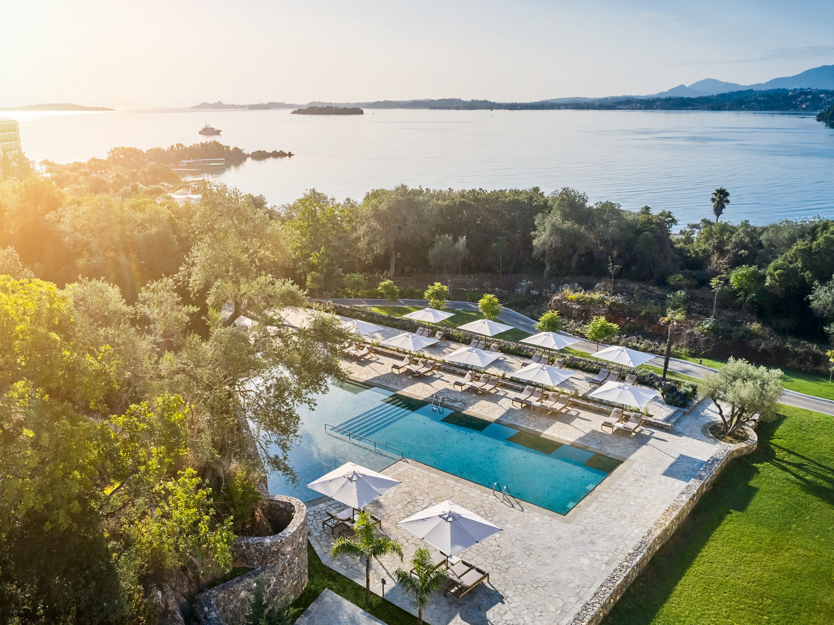 An aerial view of a resort with a swimming pool, sun loungers, and umbrellas.