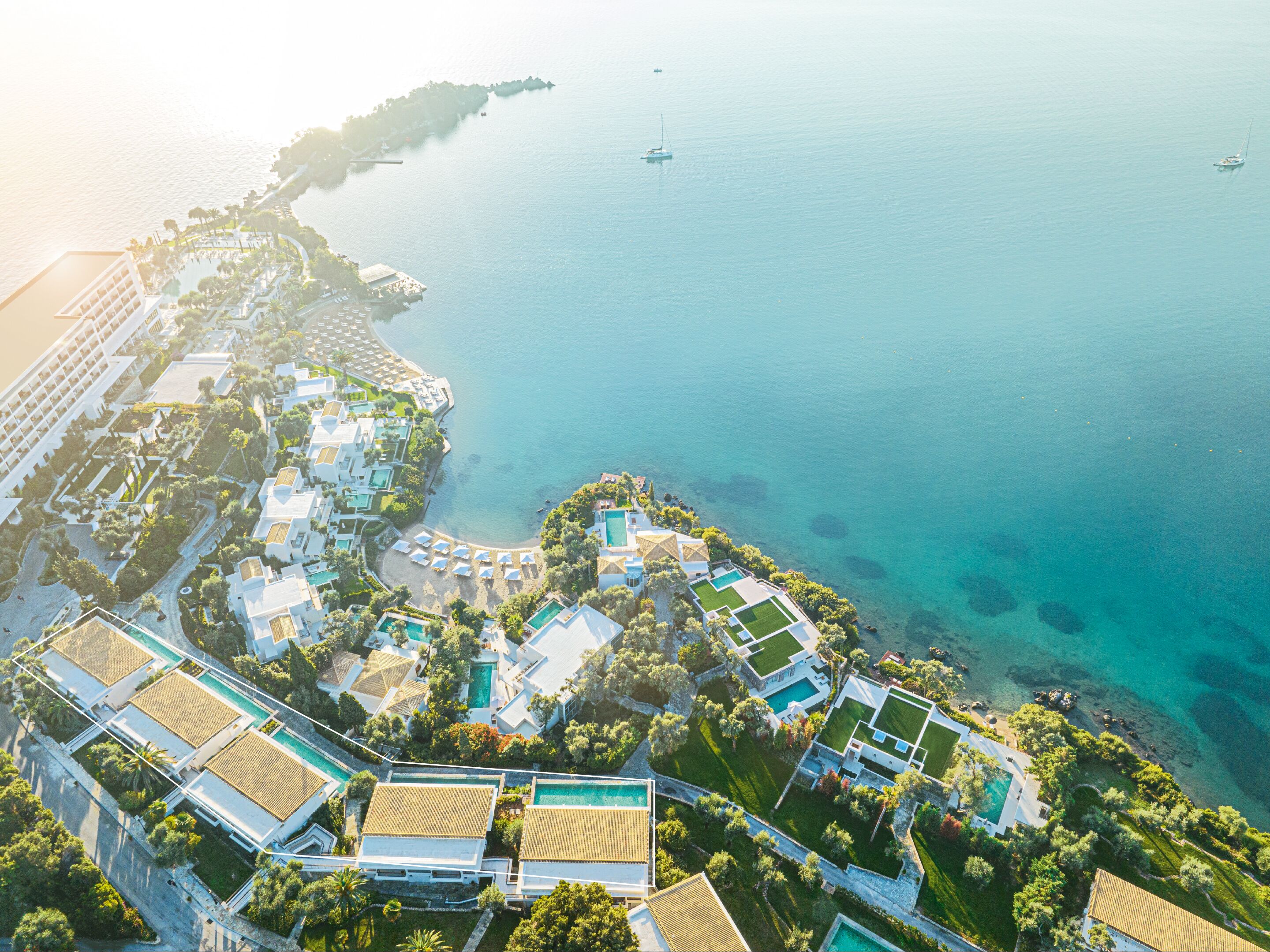 An aerial view of a coastal resort with multiple buildings, clear blue waters, and a small island in the distance.