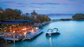A waterfront property with a dining area, lounge chairs, and a boat docked by the water.