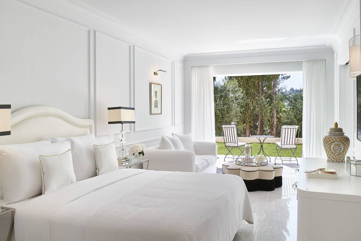 A hotel room with a large bed, a sitting area with a table, and a view of the outdoors.