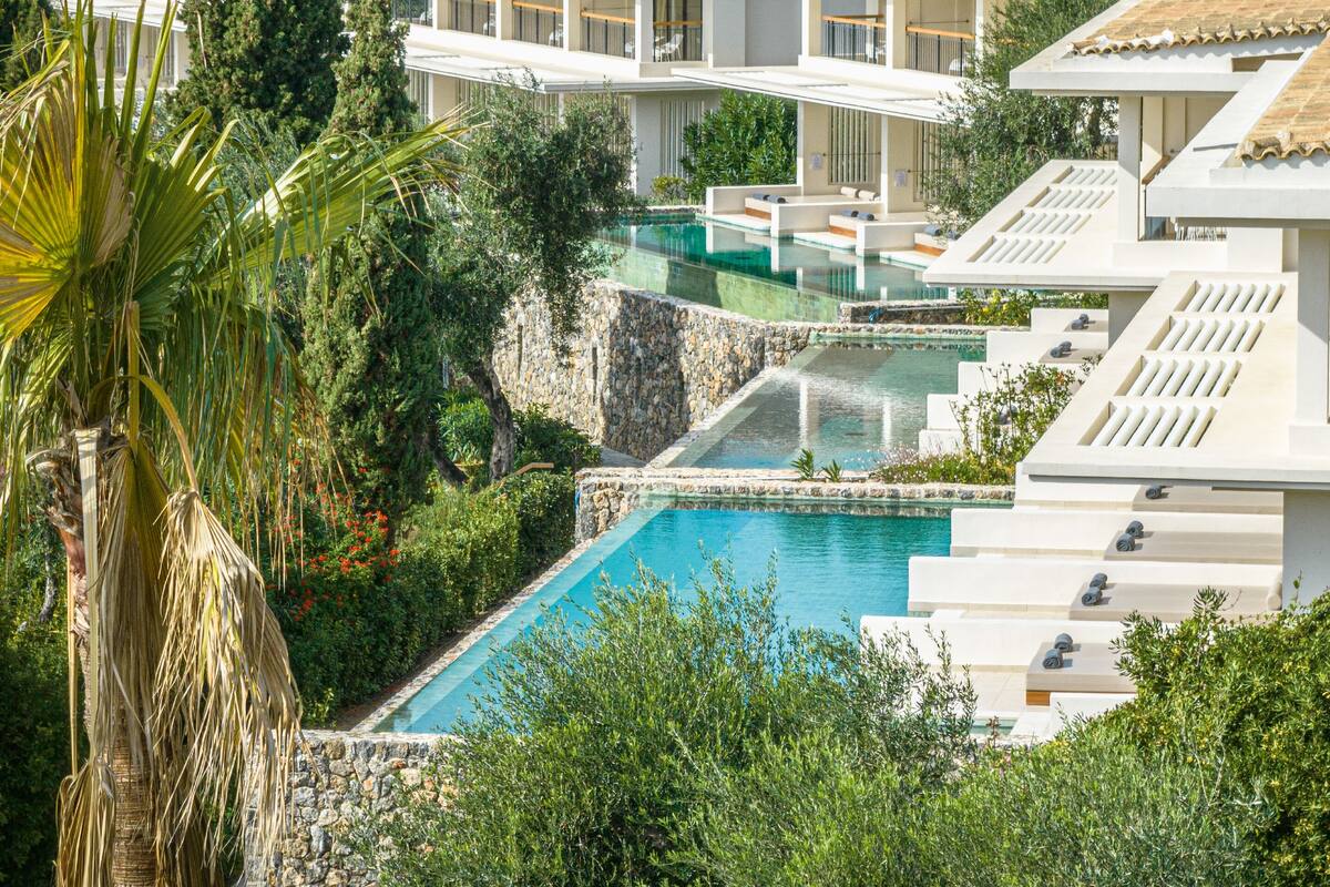 A modern hotel with a pool, outdoor seating, and lush greenery.