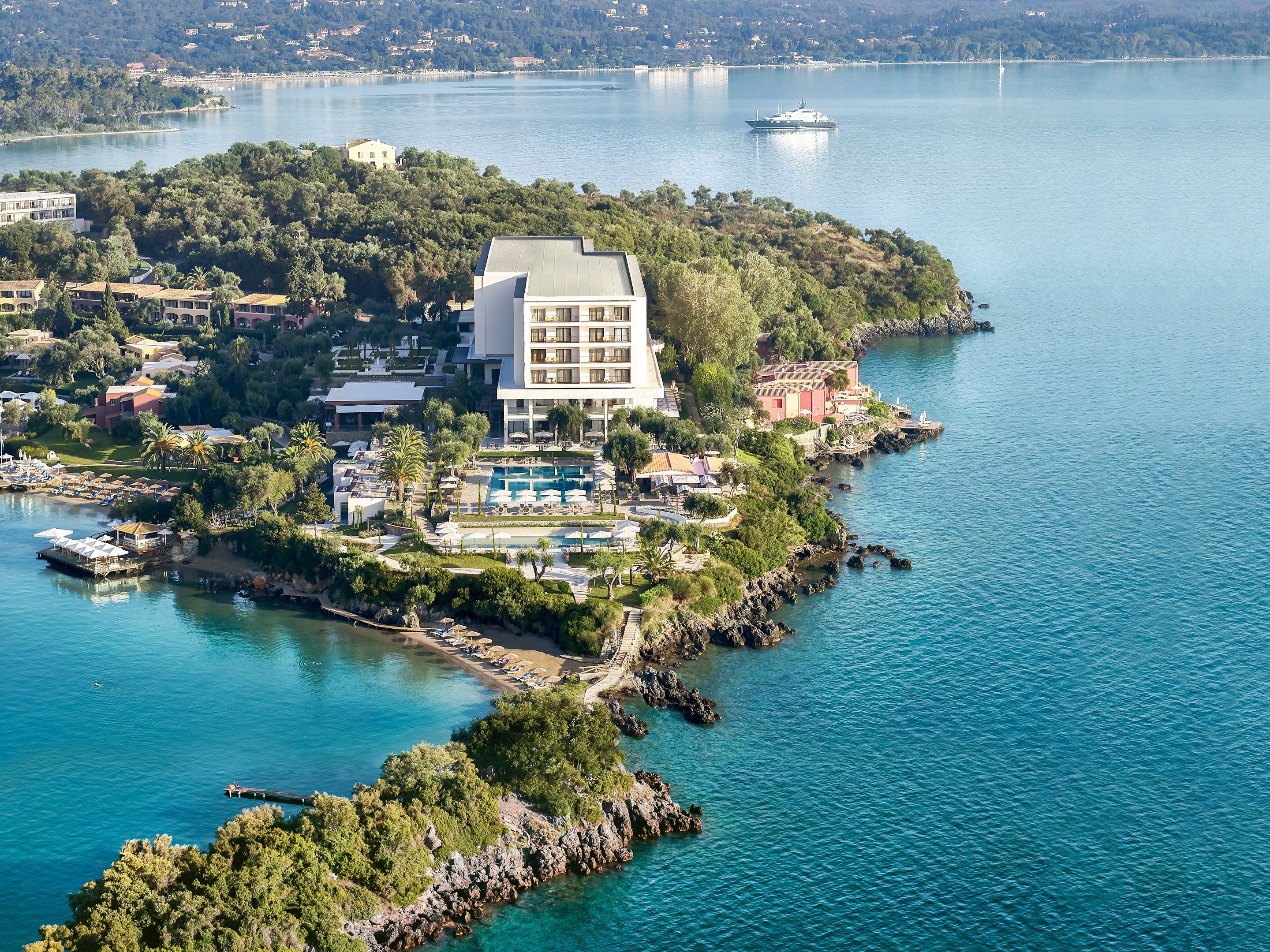 An aerial view of a coastal resort with a large building, a swimming pool, and a marina.