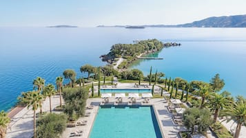 A resort with a large pool, sun loungers, palm trees, and a view of the sea.