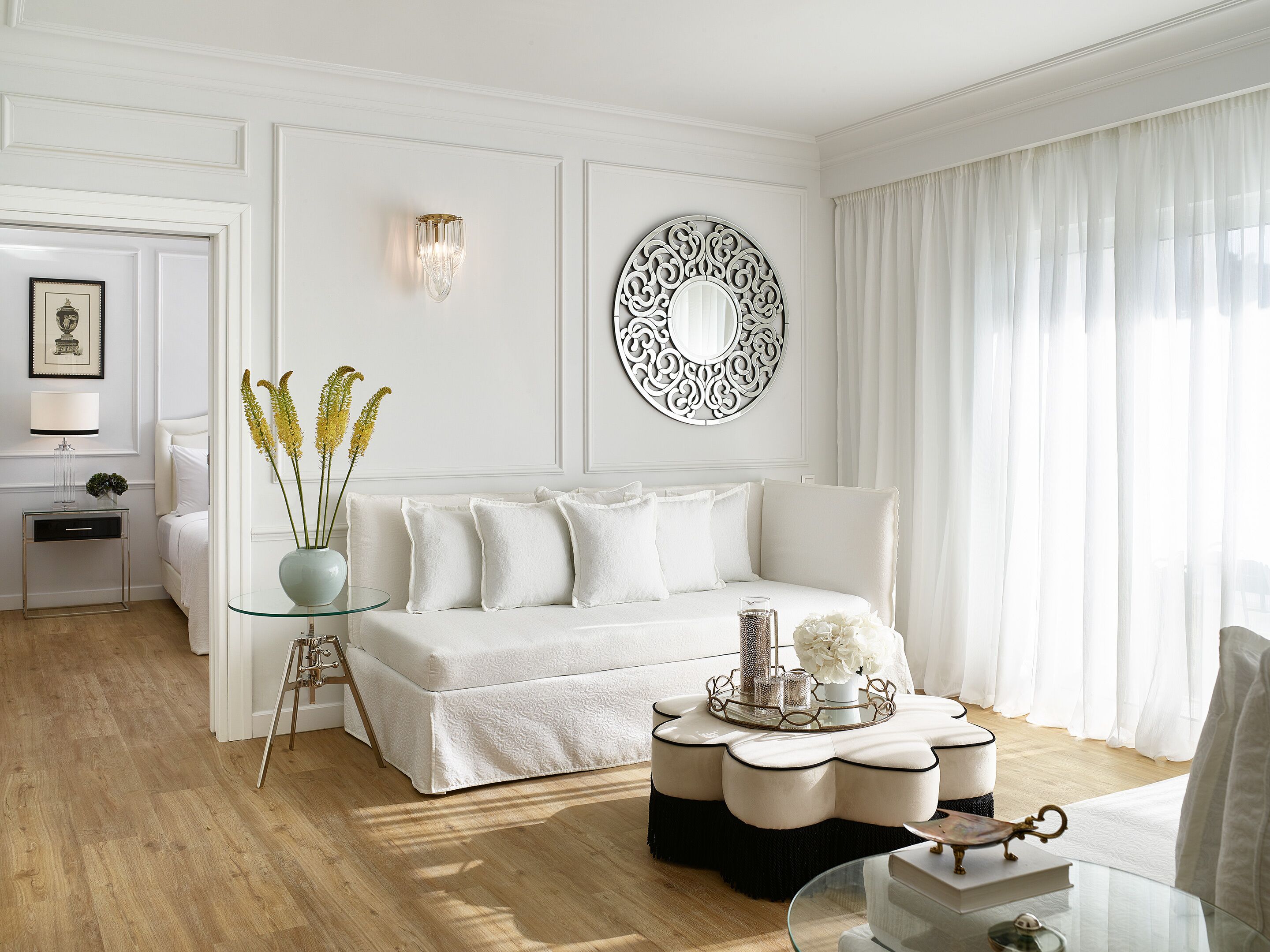 A modern living room with a white sofa, a glass coffee table, and a decorative mirror.