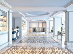 A spacious hotel lobby with a marble floor, a central staircase, and a reception area with shelves of toiletries.