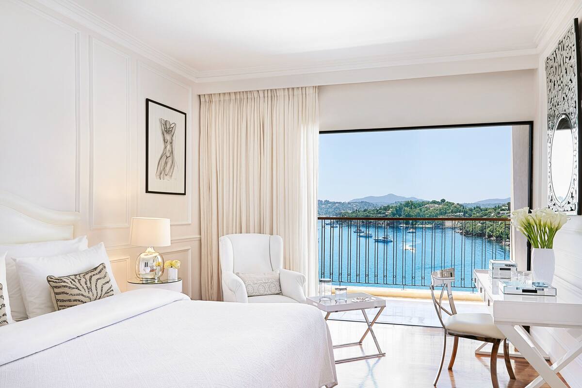 A hotel room with a large bed, a desk, and a view of a harbor with boats.