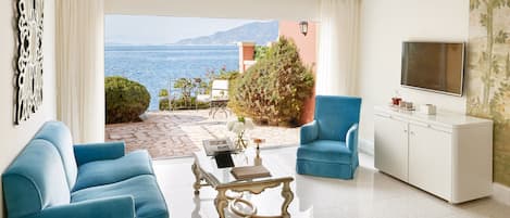 A hotel room with a large window offering a view of the sea, a sofa, a coffee table, and a TV.
