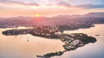 An aerial view of a coastal town with a prominent hotel complex, calm waters, and a sunset in the background.