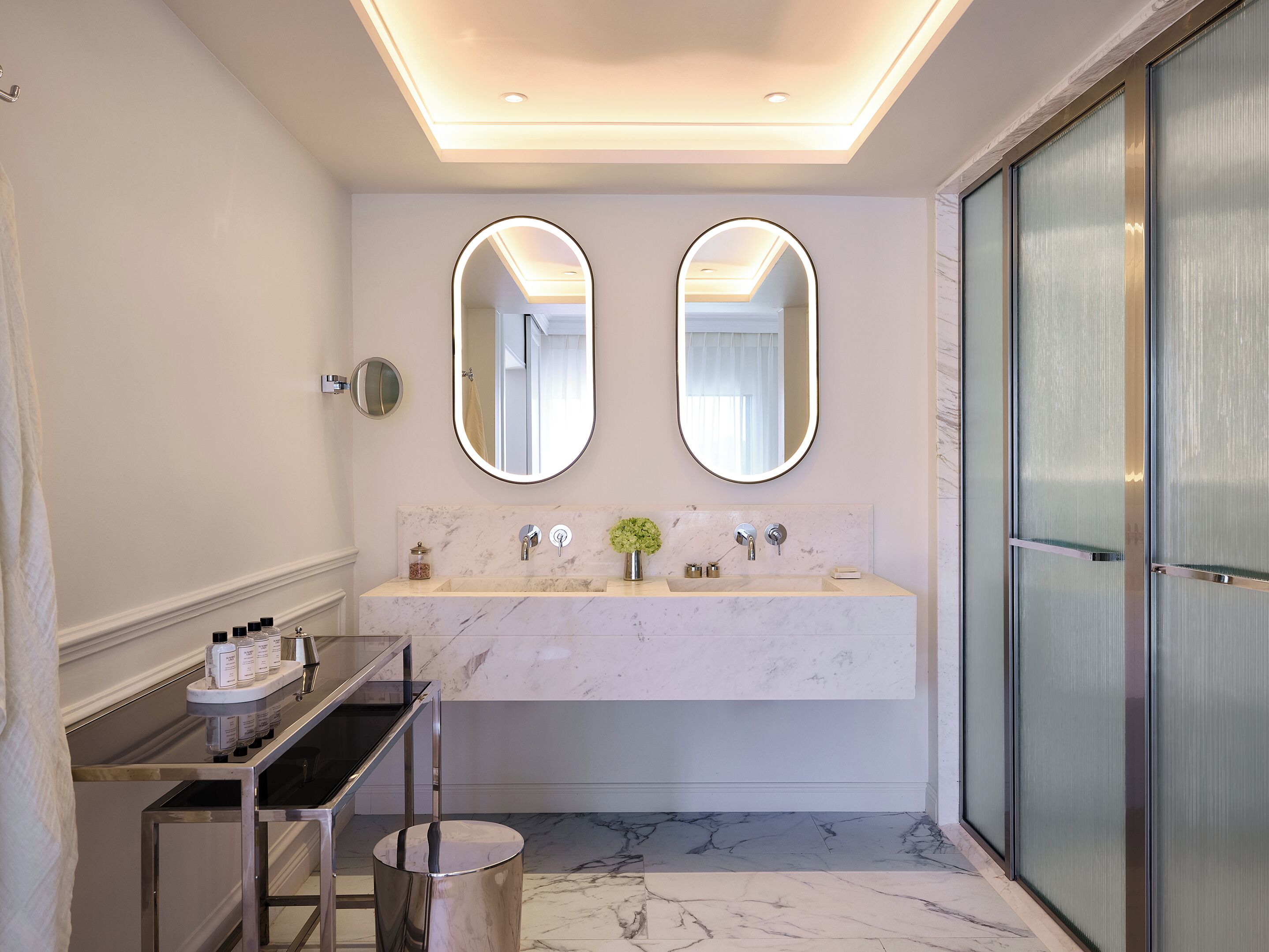 Un baño moderno con tocador de mármol, dos espejos y cabina de ducha de vidrio.
