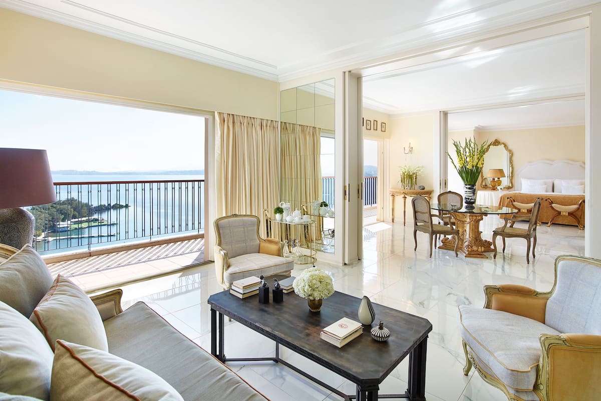 A spacious living area with a balcony overlooking a body of water, furnished with a sofa, armchairs, and a coffee table.