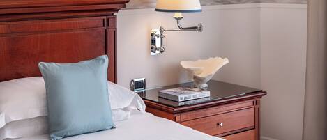 Una cama bien hecha con un almoháron azul claro, una mesita de noche de madera con una lámpara y un libro titulado 'The Amalfi Coast'.