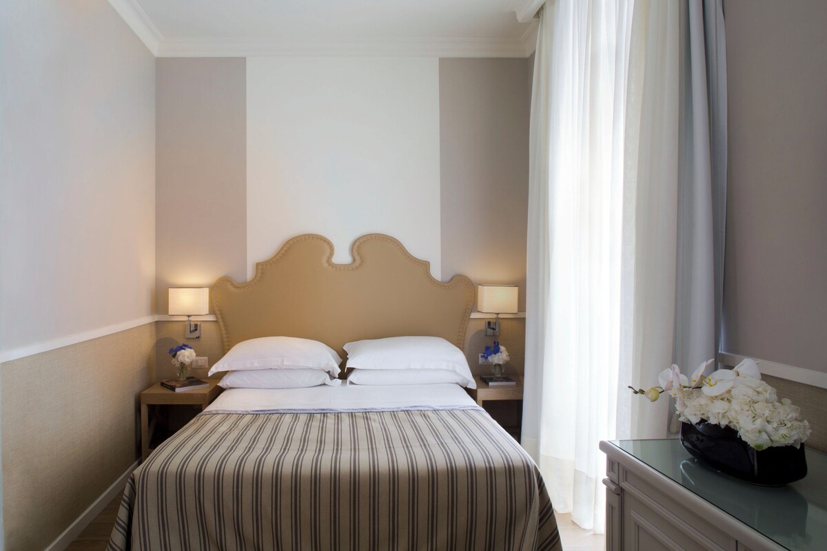 Una habitación de hotel con una cama grande, dos mesitas de noche y un ventanal con cortinas.