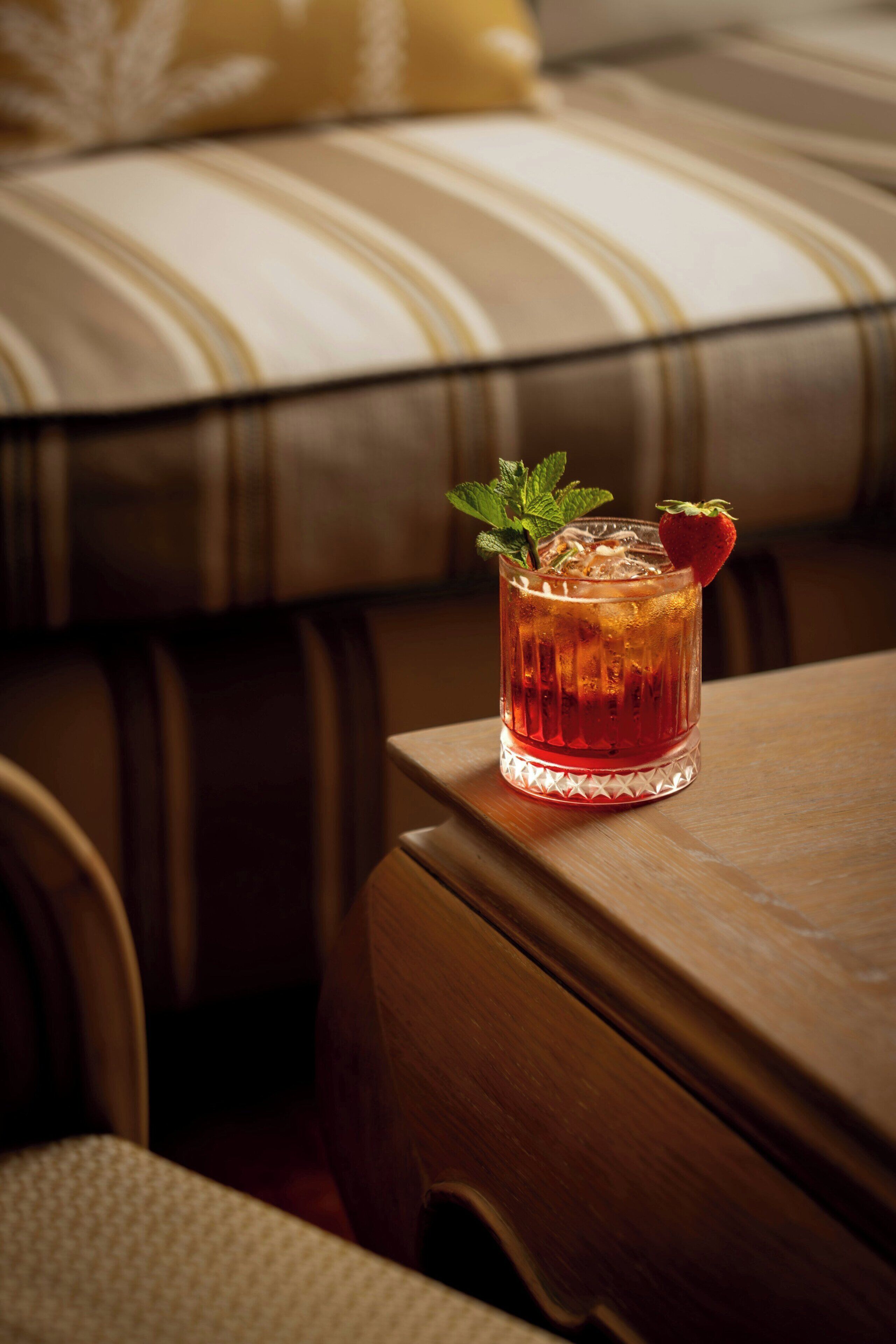 A glass of amber-colored beverage with a strawberry garnish on a wooden table.