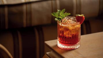 A glass of amber-colored beverage with a strawberry garnish on a wooden table.