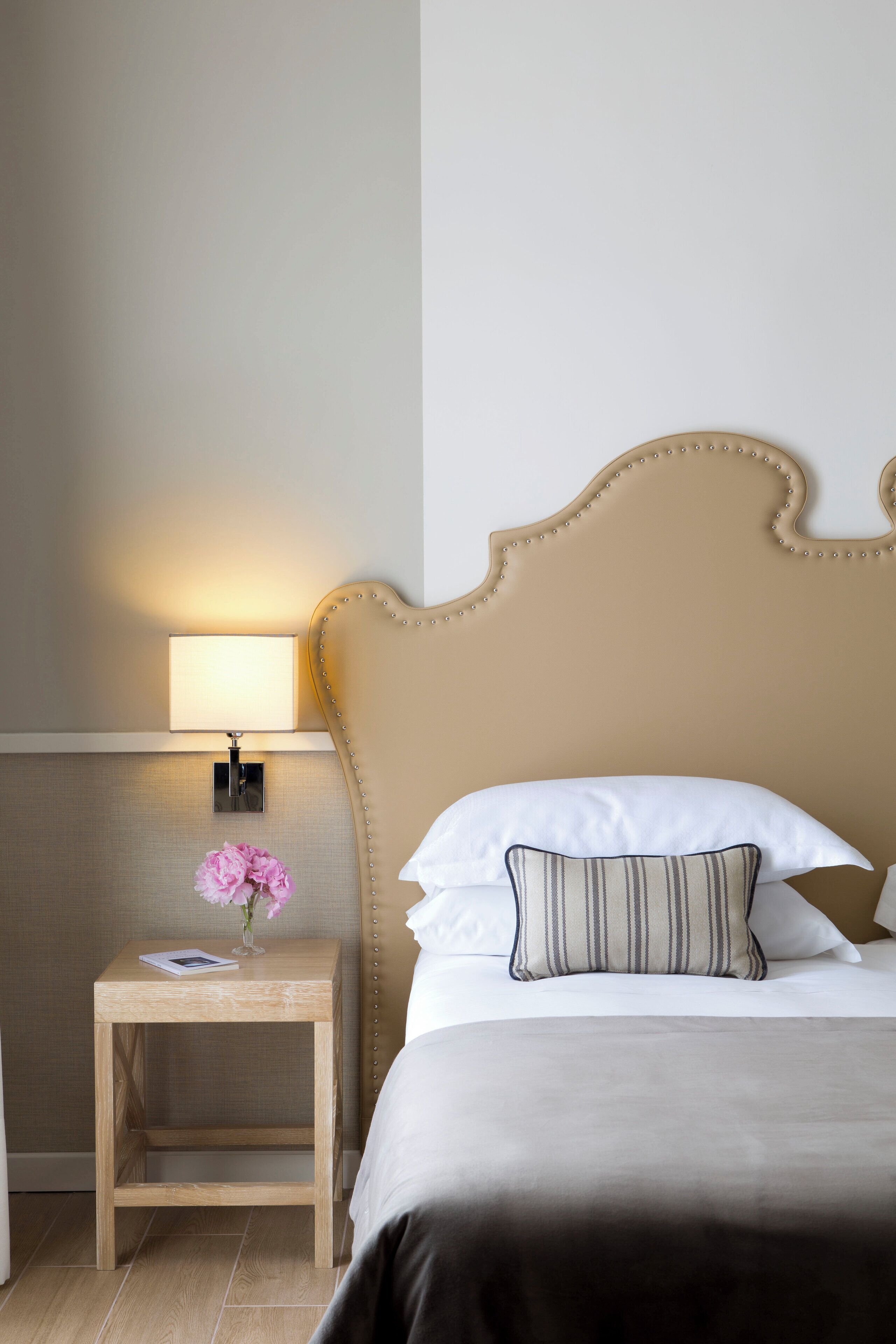 A hotel room with a bed, a nightstand with a lamp, and a vase with flowers.