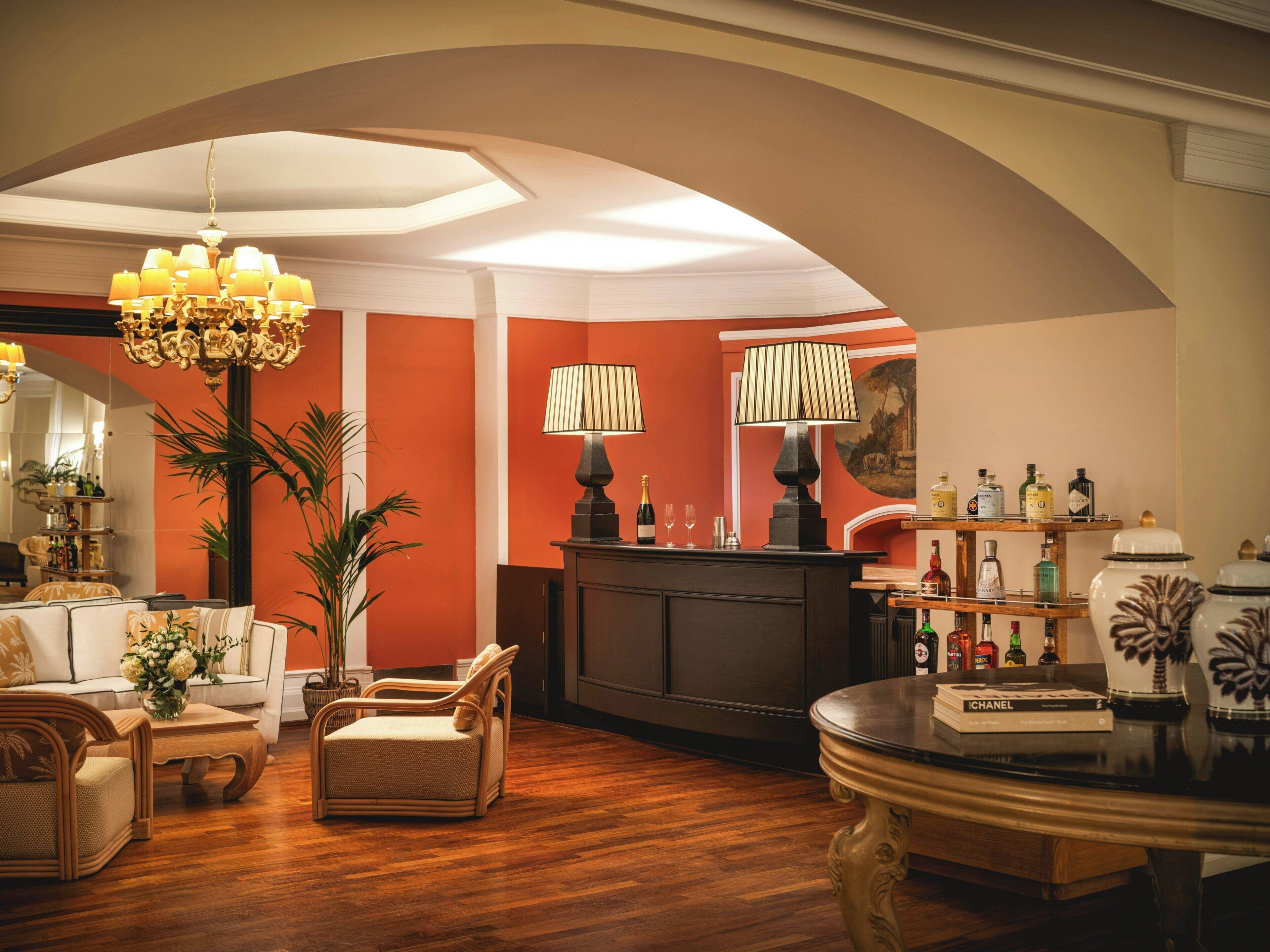A well-lit, elegantly furnished living room with a wooden floor, a chandelier, and a reception desk with various items on it.