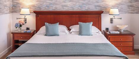 A large bed with a wooden headboard, two bedside tables with lamps, and a floral arrangement on one table.