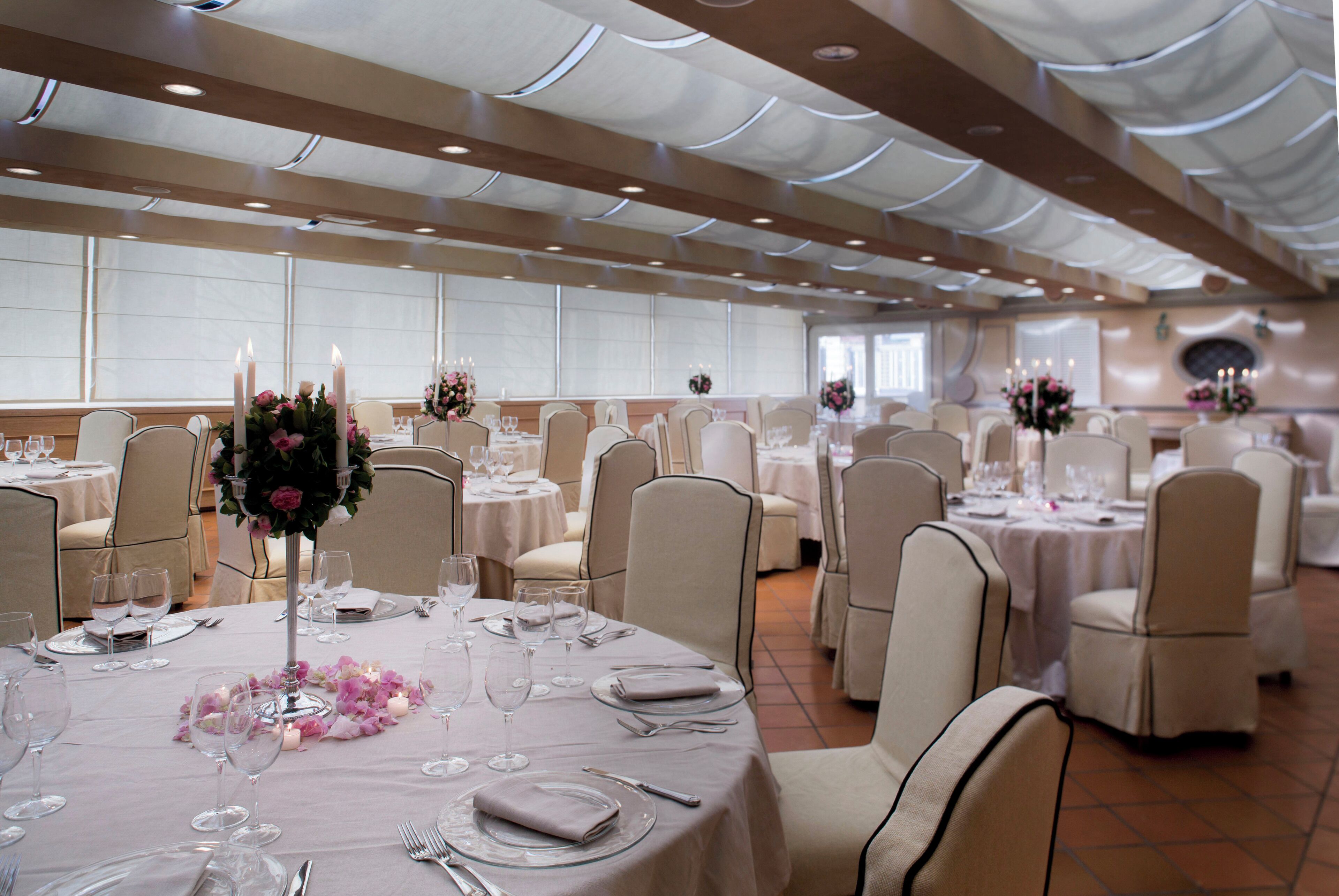 Een feestzaal met ronde tafels, elk gedekt met witte tafellakens, kaarsen en bloemstukken.