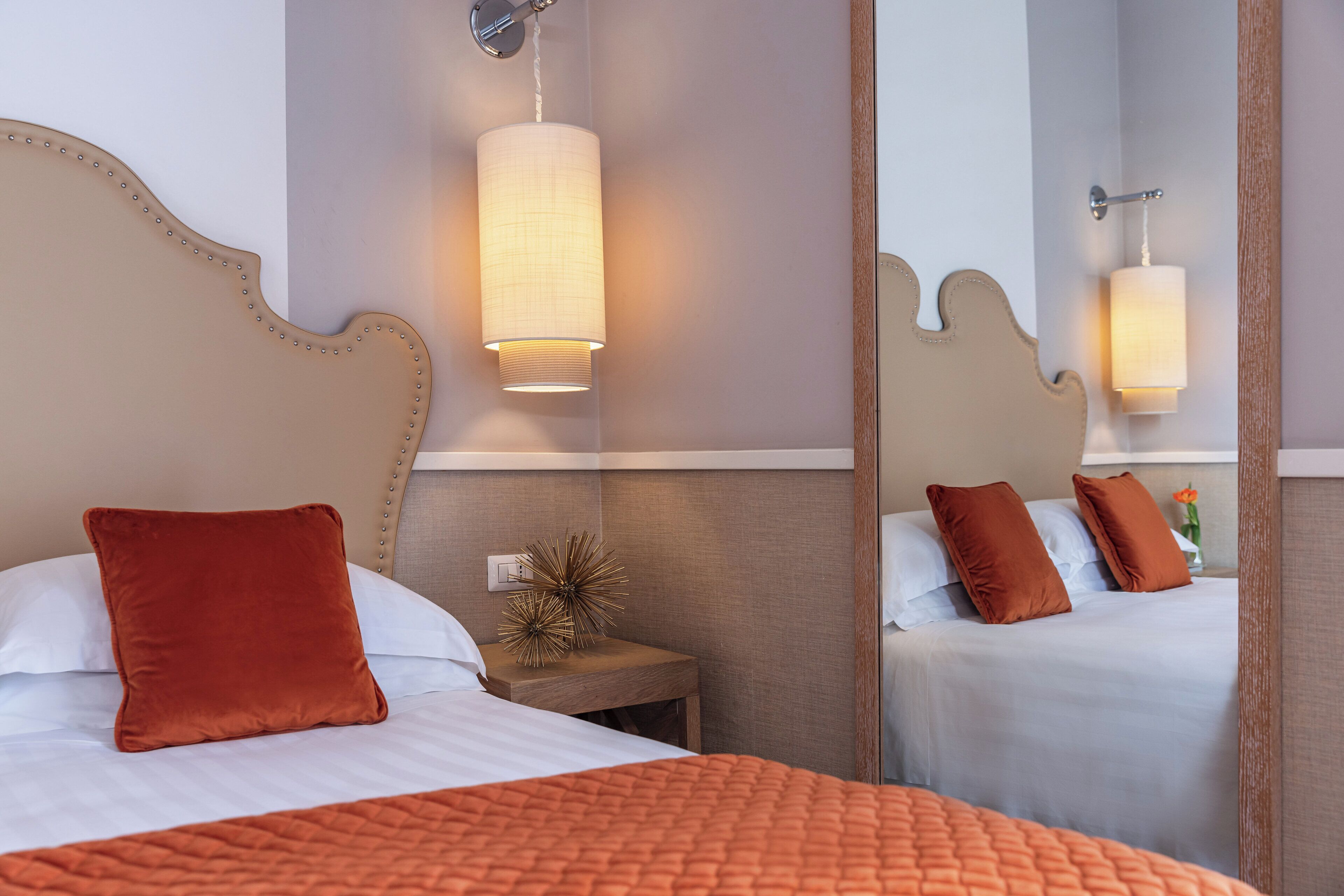 Habitación de hotel con una cama grande, una mesita de noche, un espejo y una lámpara de pared.