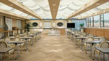 A conference room with a herringbone floor, multiple tables, chairs, a large screen, and a view through the windows.