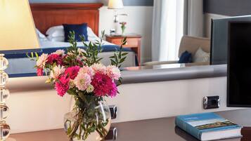 Una camera d'albergo con un letto, un comodino con una lampada, un vaso di fiori e un libro sul tavolo.