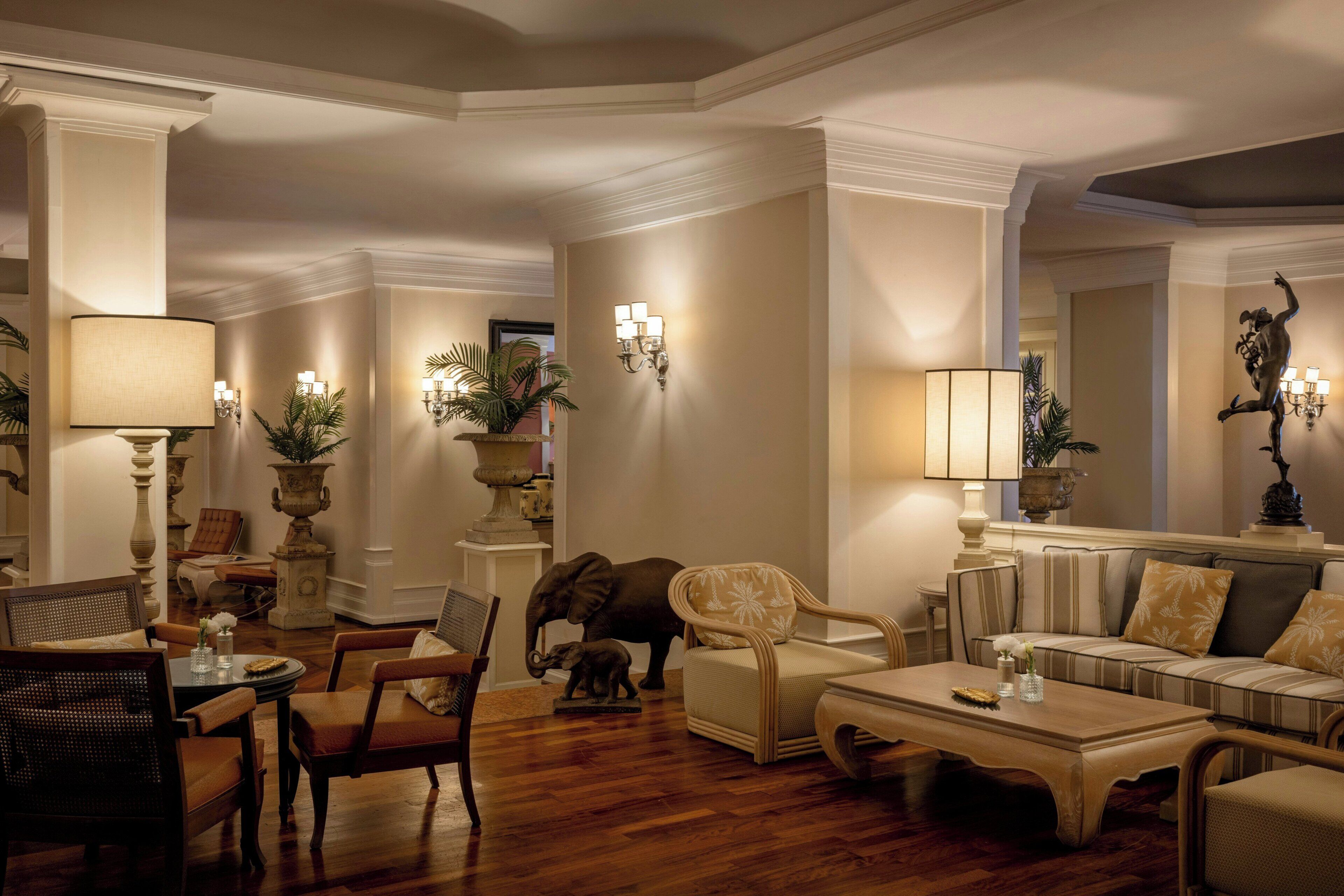 A spacious living room with a high ceiling, elegant furniture, and decorative wall sconces.