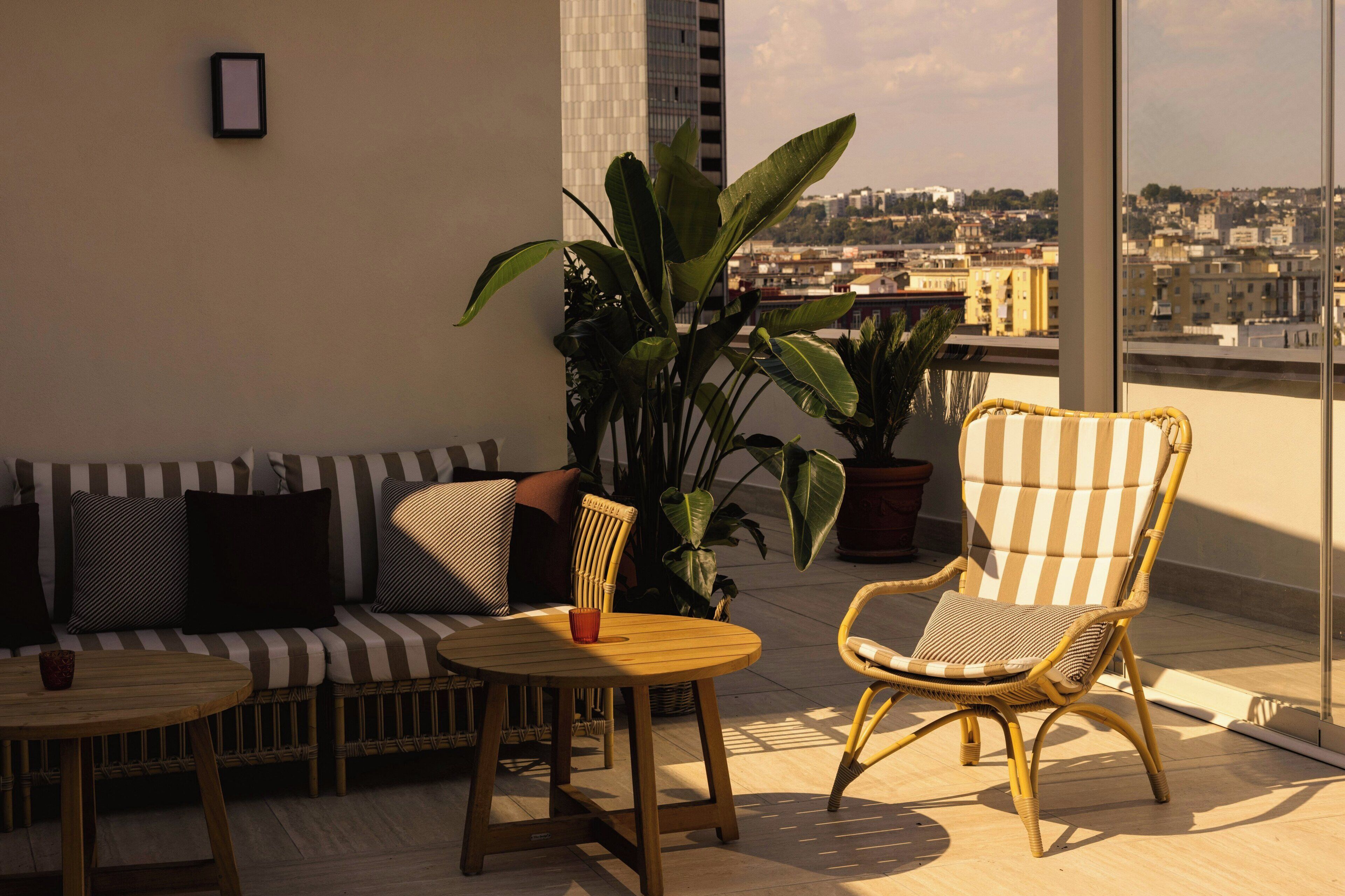 A balcony with a sofa, a chair, a small table, and potted plants.