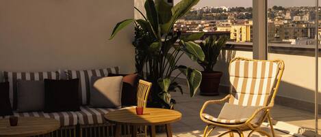 A balcony with a sofa, a chair, a small table, and potted plants.