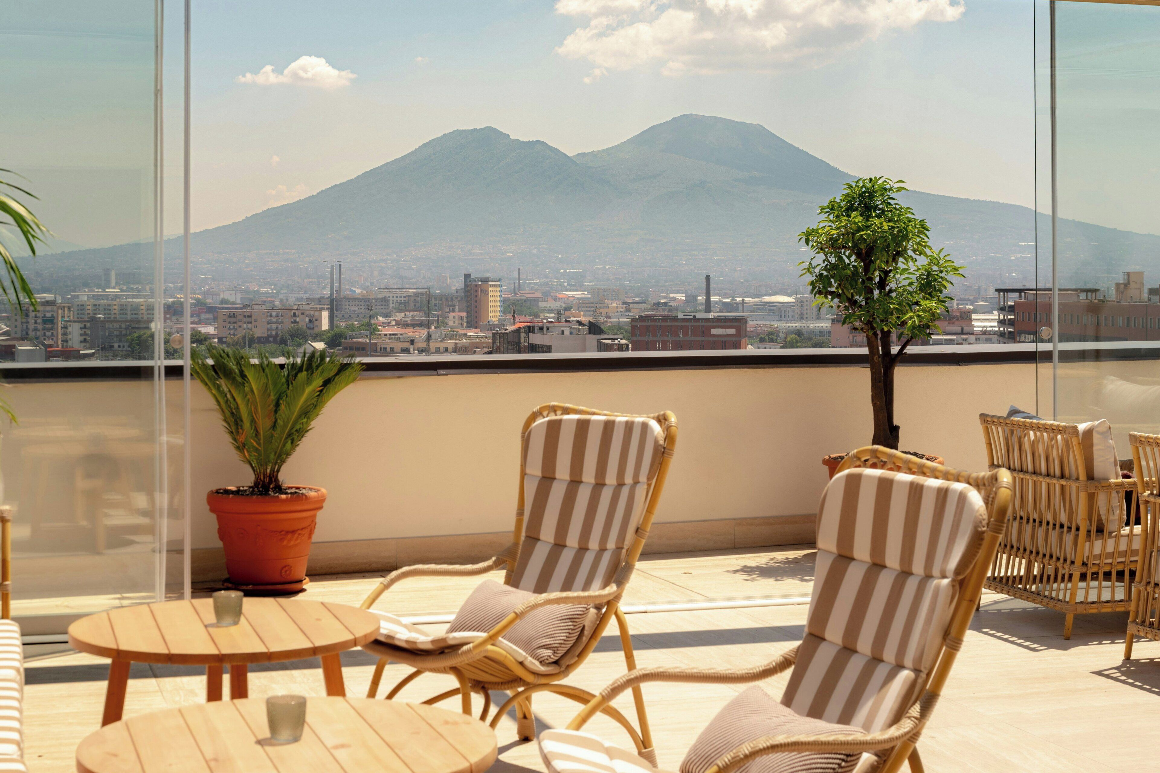 Een balkon met rieten stoelen, een tafeltje en een potplant.