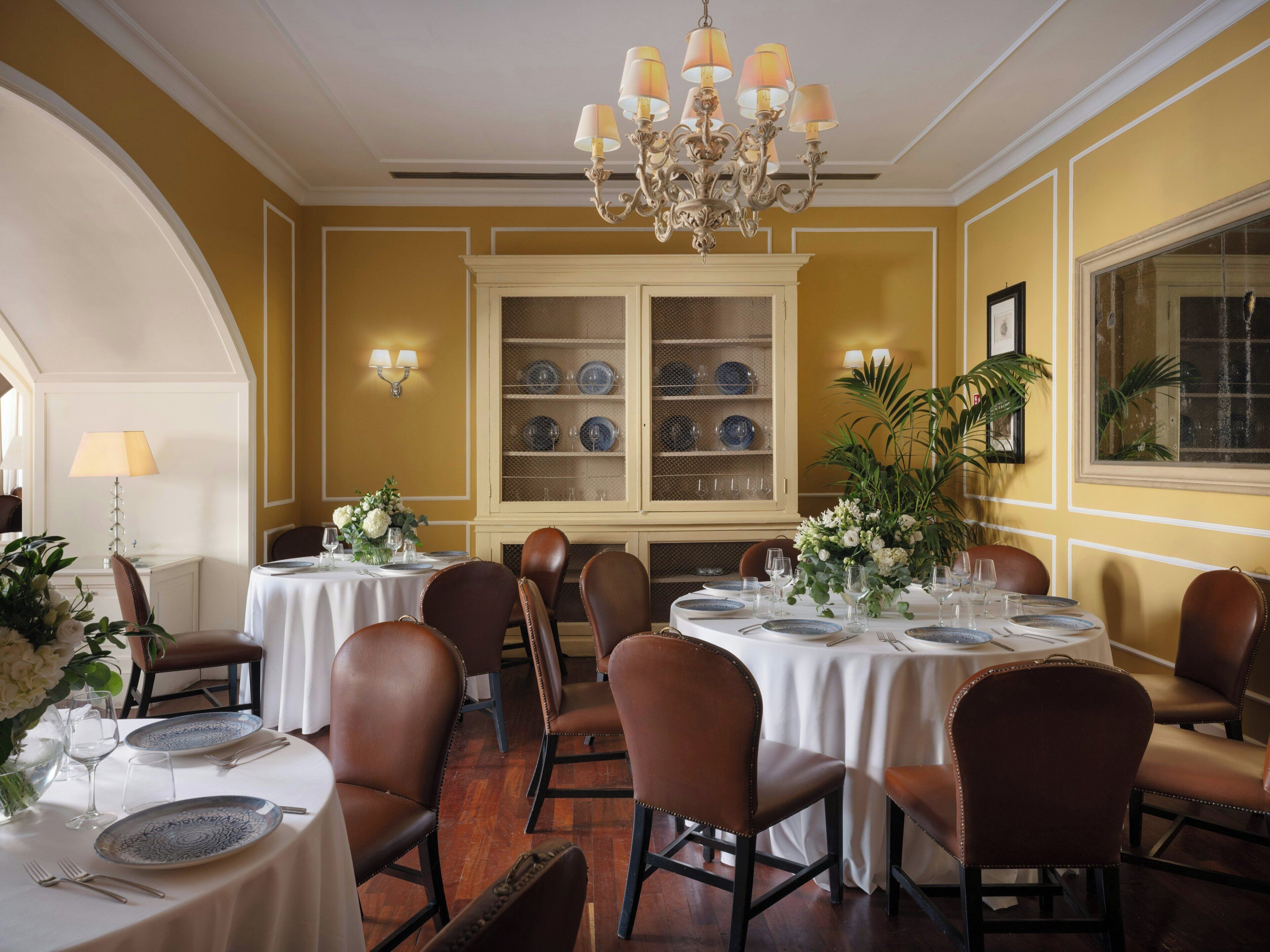 Un espace repas avec des tables rondes, des chaises en cuir marron et un lustre.