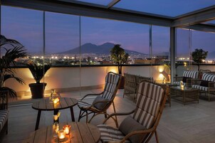 Une terrasse sur le toit, aménagée avec des meubles en osier, une table décorée de bougies et offrant une vue sur le paysage urbain et les montagnes.
