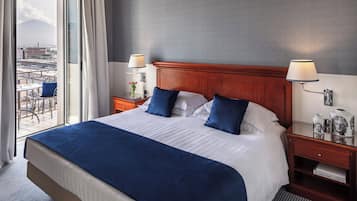 A hotel room with a large bed, two bedside tables, a view of the city, and a balcony.