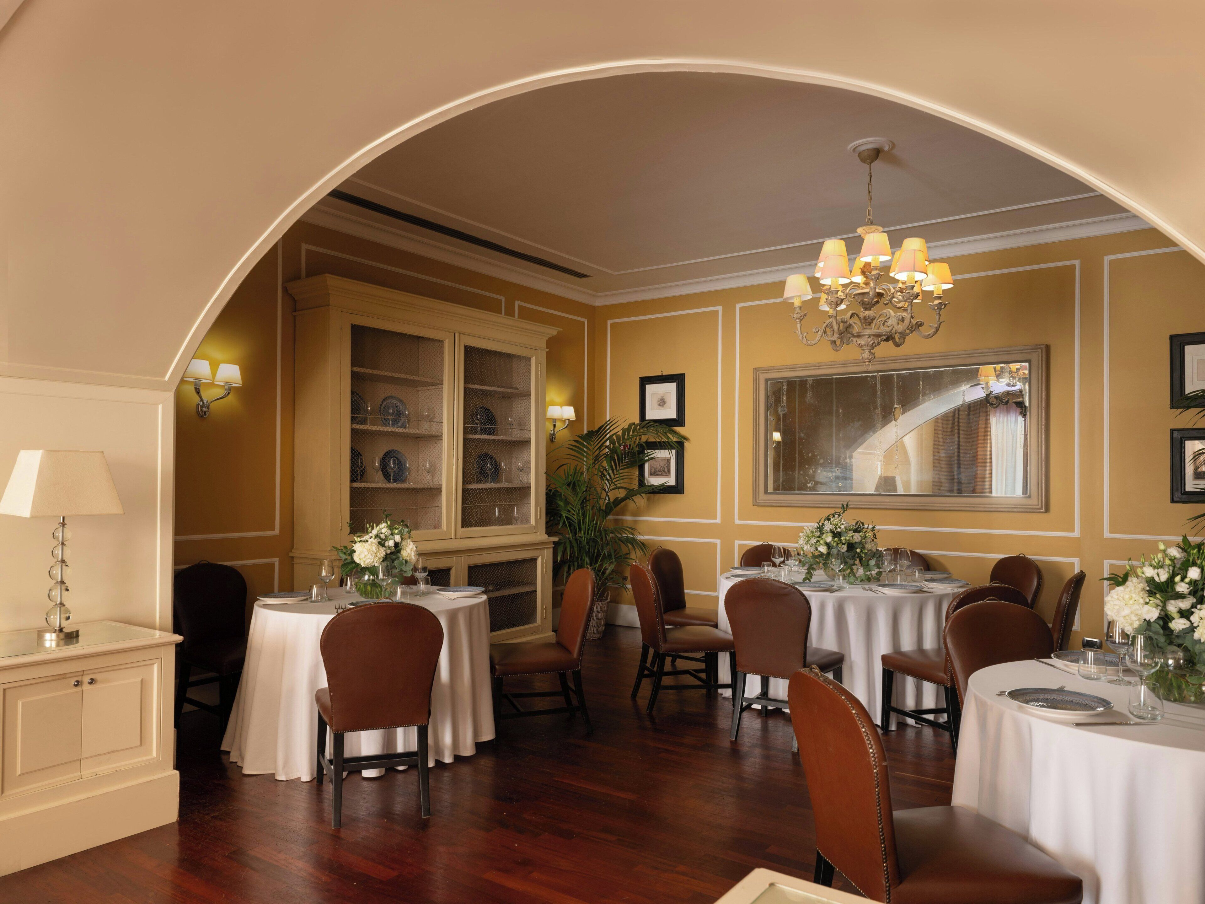 A dining area with multiple tables and chairs, a large arched doorway, and a chandelier.