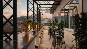 A rooftop terrace with a city view, potted plants, and outdoor seating.