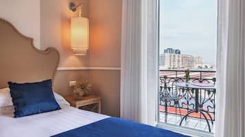 Ein Hotelzimmer mit einem großen Bett, einem Nachttisch, einer Wandlampe und einem Balkon mit Blick auf die Stadt.