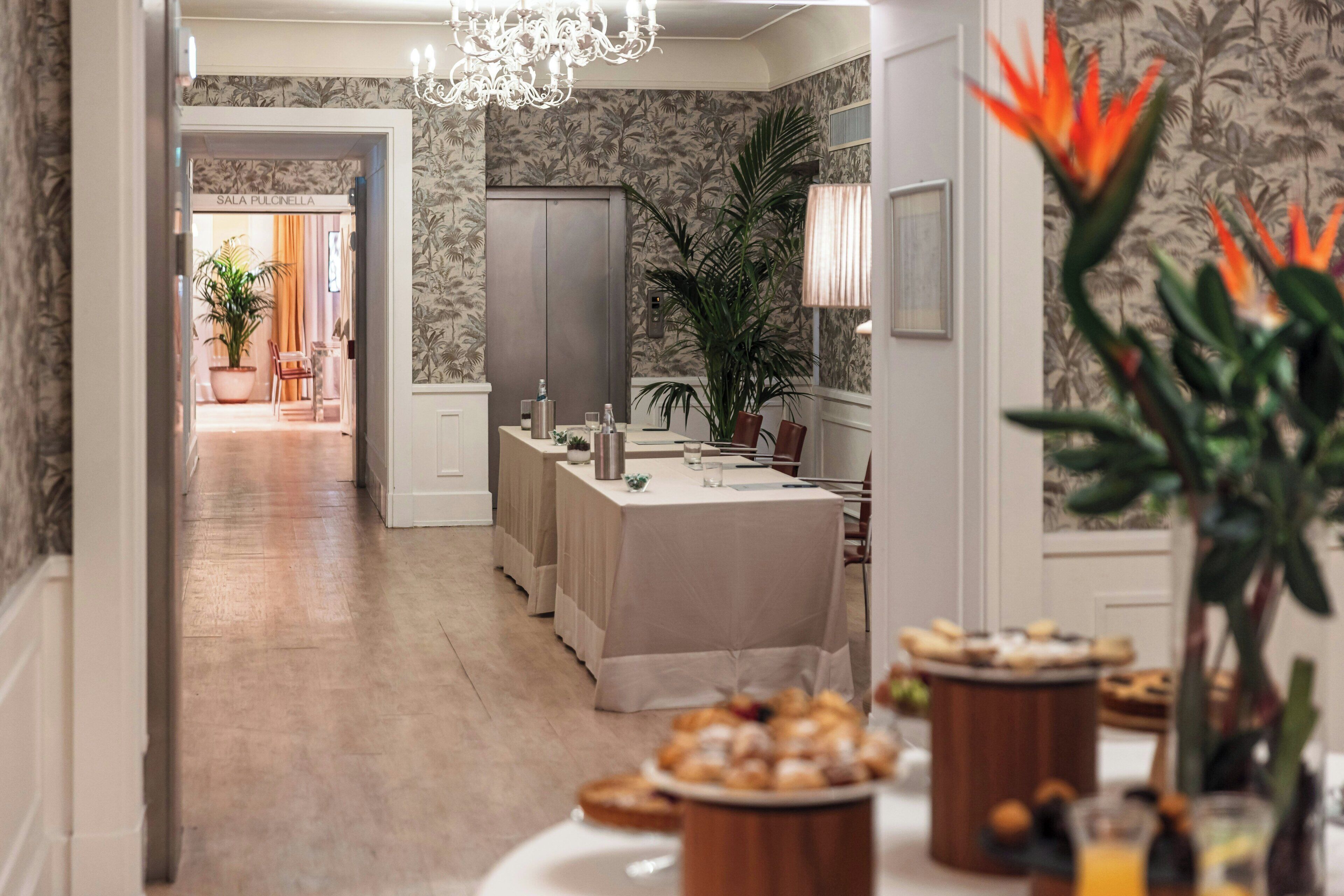 A hotel lobby with a reception desk, a large plant, and a dining area with a buffet.