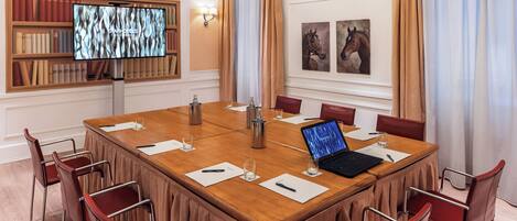 A conference room with a large table, chairs, a laptop, and a TV screen.