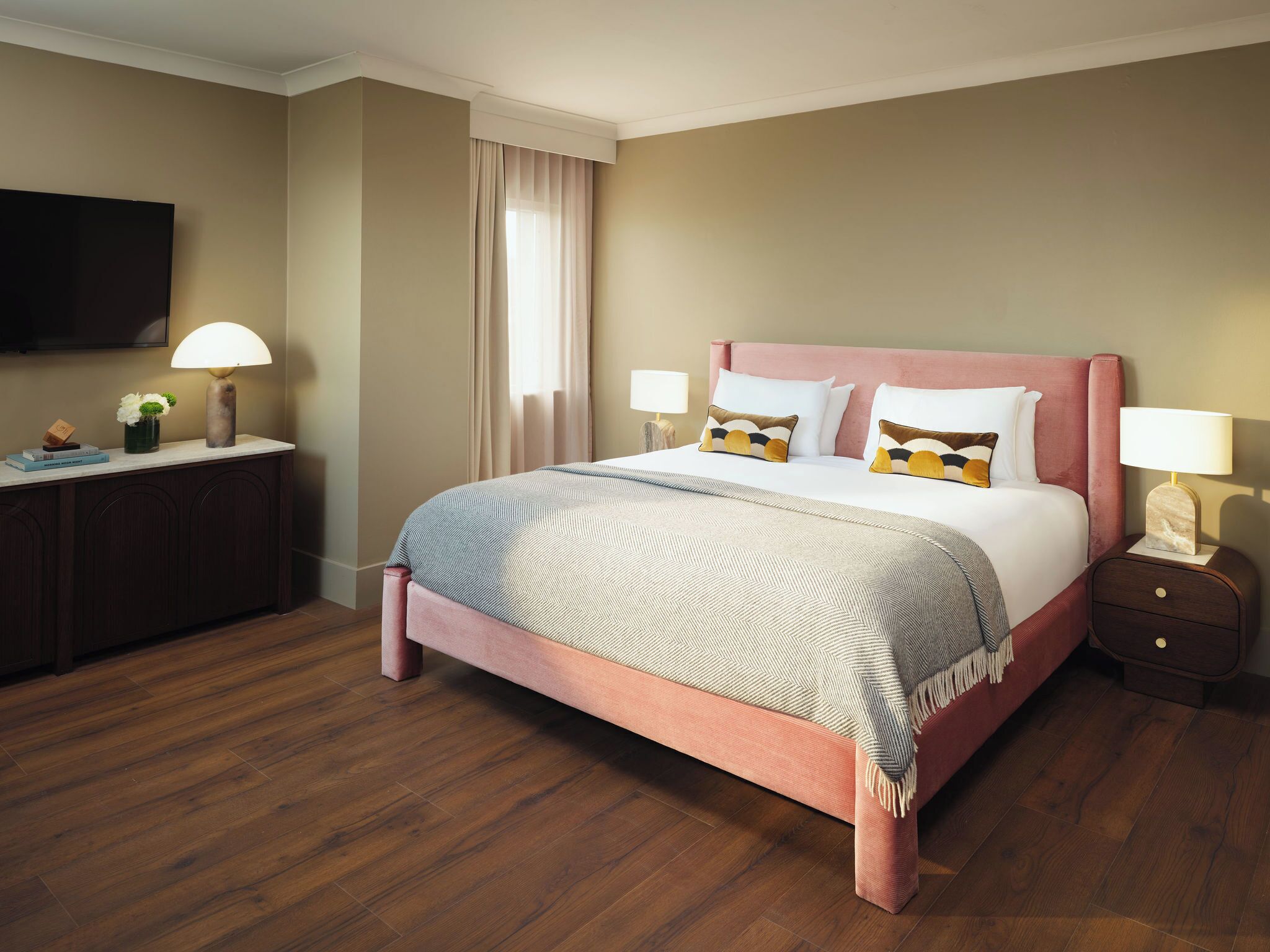 A neatly arranged hotel room with a bed, bedside tables, a desk, and a TV.